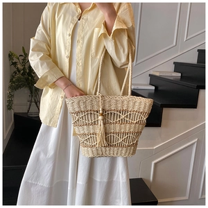 Detail of hand-woven straw tote bag featuring long tassel charms and openwork texture