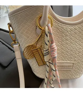 Vue détaillée du sac seau tissé beige avec breloques dorées et plaque de logo en métal poli