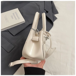 Detailed side view of beige leather Kelly bag with heart charm and crossbody strap