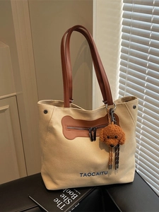 Large beige canvas tote bag with brown leather straps and a cute plush puppy charm