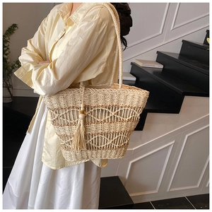 Detail of woven straw tote bag featuring decorative fringe and wooden bead tassels