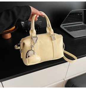 Detailed view of cream yellow patent leather Boston bag with silver heart charm and strap