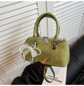 Detail der grünen Boston Handtasche mit Perlenanhänger und weißer Spitzenschleife