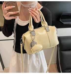Detail of light beige bowling bag with heart charm and shoulder strap in lifestyle setting
