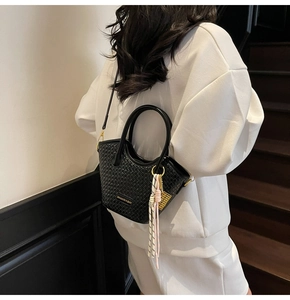 Détail du sac seau tissé noir avec plaque logo dorée et breloque pompon en corde chic