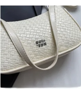 Close-up of woven texture and silver metal logo on an elegant off-white underarm bag