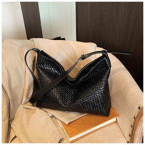 Detail of glossy black woven tote bag with adjustable strap on a soft lounge chair