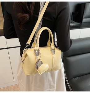 Detail of cream Boston handbag with leather heart charm and golden chain on handle
