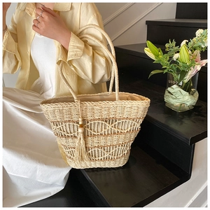Close-up of beige woven straw tote bag with hollow patterns and tassel decoration
