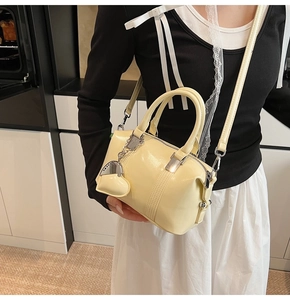 Detail of cream mini Boston bag with glossy patent finish and silver heart pendant