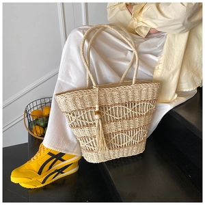 Detail of hand-woven straw tote bag with wave hollow pattern and tassel wooden bead charm