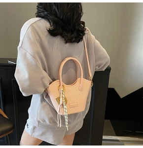 Détail d'un sac seau tressé rose avec poignée et bandoulière porté par un mannequin