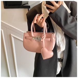 Detail of pink mini shell bag with silver buckle, heart pendant, and glossy leather finish