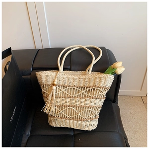Close-up of beige woven straw tote bag with diamond pattern and tassel bead charm