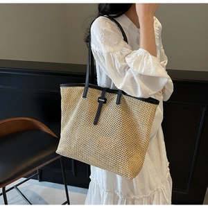 Détail d'un sac cabas en paille avec bandoulière en cuir noir et boucle sur un modèle