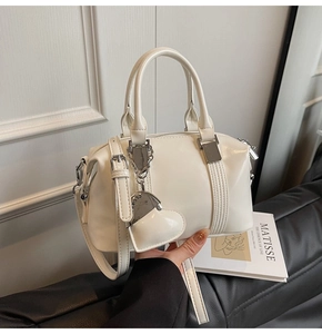 Detail of white PU leather crossbody bag featuring silver heart charm and top handle
