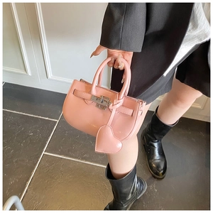 Detail of pink patent leather handbag featuring heart charm and metal twist lock