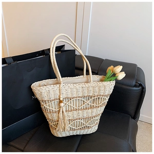Detail view of woven straw tote bag with diamond cutout patterns and wood bead tassel charm