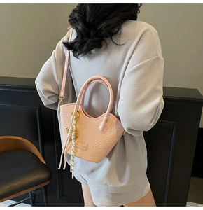 Detail of pink faux crocodile leather bucket bag with braided fringe accessory and long strap