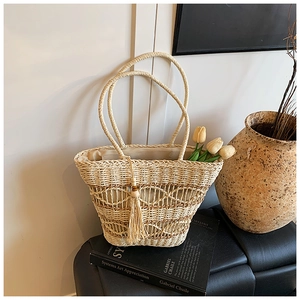 Detail of hand-woven straw tote bag with tassel fringe on a minimalist background