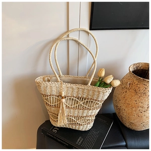 Detail of hollow woven straw tote bag with tassel charm and beige lining for summer holiday