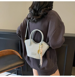 Detail of light blue woven bucket bag with tassel charm and gold brand plate