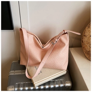Macro view of pink woven leather shoulder bag resting on silver luggage case
