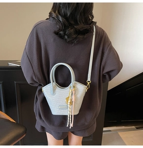 Detail of light blue woven bucket bag with elegant tassels and slim shoulder strap