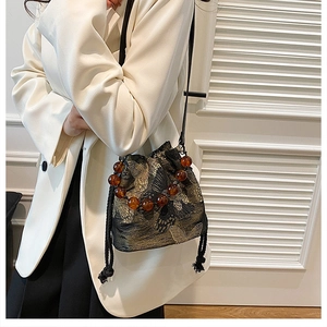 Detail of embroidered butterfly bucket bag with amber bead handle and leather strap