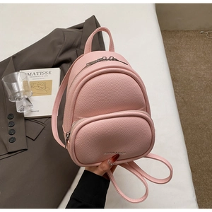 Pink mini backpack in litchi grain PU leather held against a stylish office outfit