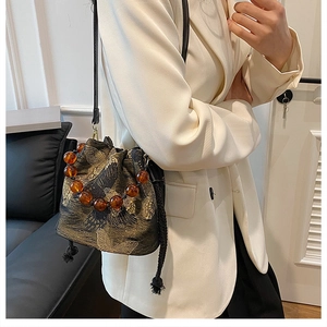 Detailed view of butterfly embroidery and amber beaded handle on a black bucket bag