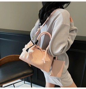 Pink woven bucket bag with white bow charm and small zip pouch on a leather chair