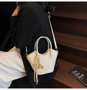 Detail of cream woven bucket bag featuring metal abacus charm and fringe tassel detail