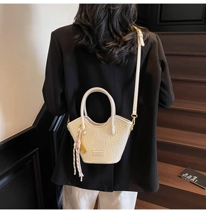 Detail of cream woven bucket bag with elegant tassels and gold hardware on model