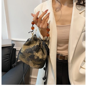 Detail of butterfly embroidery bucket bag featuring amber bead handle and drawstring close