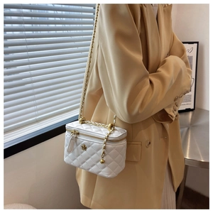 Close-up of a white quilted bucket bag with golden chain strap and floral charm detail