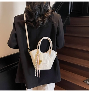 Detail of cream woven bucket bag with tassel pendant and detachable shoulder strap