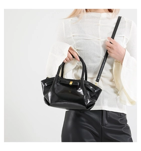 Detail of black pleated faux leather crossbody bag featuring gold buckle and slim strap