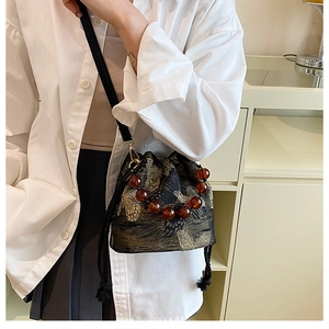Detail of butterfly embroidery on black bucket bag with amber bead handle and long strap