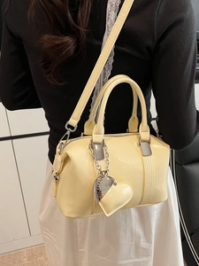 Cream yellow shiny patent leather Boston bag with silver chain heart charm on a model