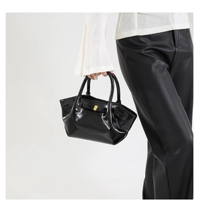 Detailed macro view of black patent leather motor bag with golden buckle and handle