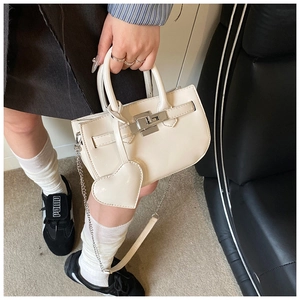 Detail view of off-white shell handbag with silver turn-lock and heart charm accessory