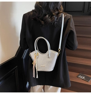 Silver woven crossbody bag with round handle and tassel detail shown on a model
