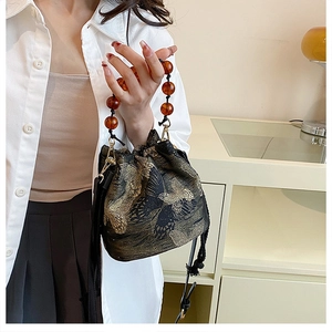 Close-up of butterfly embroidery and amber beaded handle on a black bucket bag