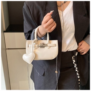 Detailed view of cream patent leather shell bag with heart charm and silver metal lock