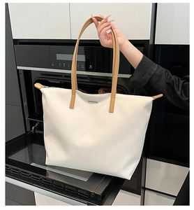 Close-up of beige tote bag with brown straps and metal logo in modern kitchen setting
