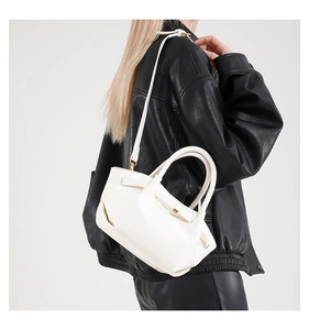 Detail of white glossy PU leather bag with gold buckle on a black leather jacket