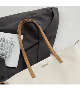 Detail of minimalist cream nylon tote bag with brown leather straps and silver metal logo
