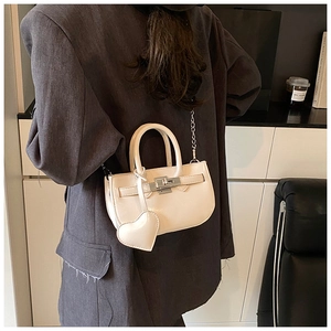 Detailed view of cream leather handbag featuring heart charm and metallic buckle closure