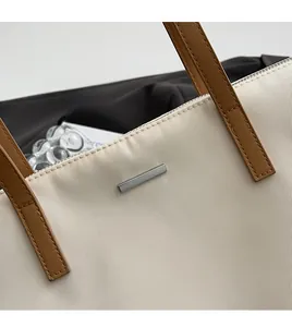 Detail of minimalist tote bag with beige fabric, brown leather handle, and silver logo plate